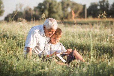 Büyükbaba ve torununun Meadow 'da kitap okurken çekilmiş bir fotoğrafı. Küçük çocuk ilk adımlarını okuyor..