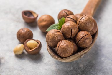 Macadamia fındıklarını istifleyin. Çekirdekleri ve kabukları taş arka planda kaşıkla açın..