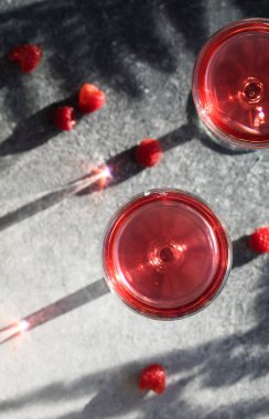 Alkollü cin kokteyli. Gri taşlı arka planda uzun ahududu içeceği, kopyalama alanı. Bir bardak kunduzun içinden gün ışığı. Güneş sert gölge yansıması