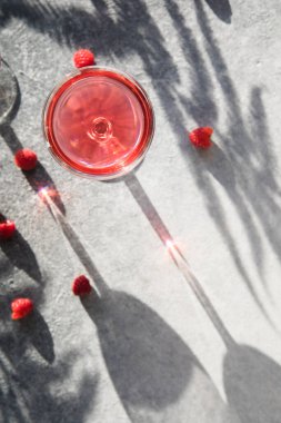 Alkollü cin kokteyli. Gri taşlı arka planda uzun ahududu içeceği, kopyalama alanı. Bir bardak kunduzun içinden gün ışığı. Güneş sert gölge yansıması