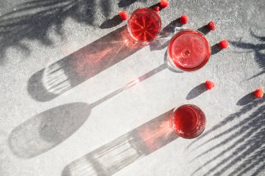 Alkollü cin kokteyli. Gri taşlı arka planda uzun ahududu içeceği, kopyalama alanı. Bir bardak kunduzun içinden gün ışığı. Güneş sert gölge yansıması