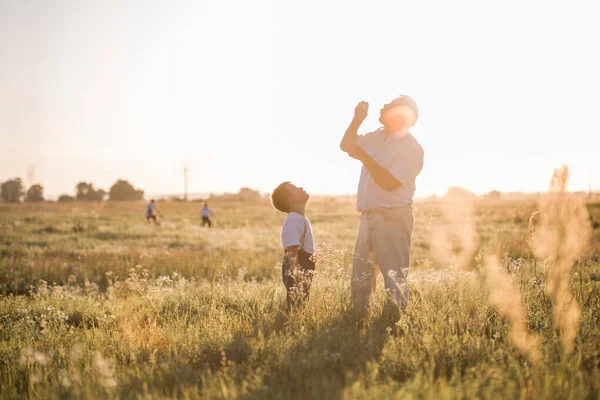 Happy senior man Grandfather with cute little boy grandson playing in field. Happy child with Grandfather playing outdoors