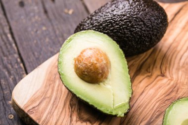 Ahşap arka planda iki Haas avokado meyvesi. Avokadoyu dilimle