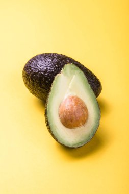 Sarı arka planda iki Haas avokado meyvesi. Avokadoyu dilimle