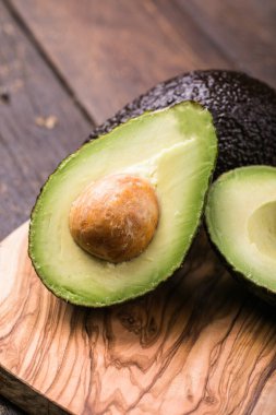 Ahşap arka planda iki Haas avokado meyvesi. Avokadoyu dilimle