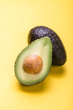 Sarı arka planda iki Haas avokado meyvesi. Avokadoyu dilimle
