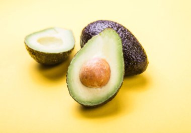 Sarı arka planda iki Haas avokado meyvesi. Avokadoyu dilimle