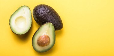 Sarı arka planda iki Haas avokado meyvesi. Avokadoyu dilimle