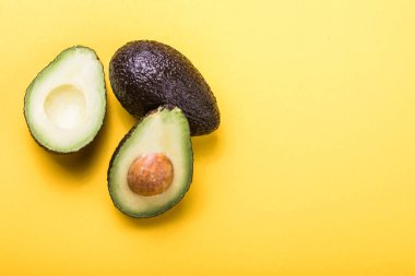 Sarı arka planda iki Haas avokado meyvesi. Avokadoyu dilimle