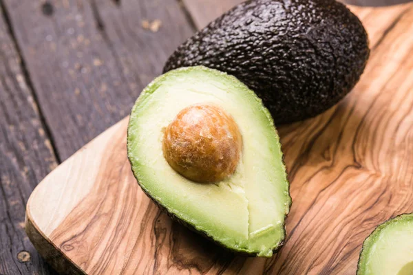 Ahşap arka planda iki Haas avokado meyvesi. Avokadoyu dilimle