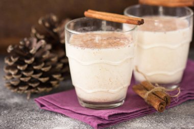 Geleneksel eggnog iki cam fincanda, üzerinde tarçın çubukları olan taş masada..