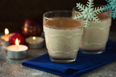 Geleneksel eggnog iki cam fincanda, üzerinde tarçın çubukları olan taş masada..