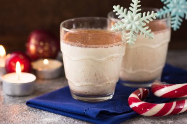 Geleneksel eggnog iki cam fincanda, üzerinde tarçın çubukları olan taş masada..