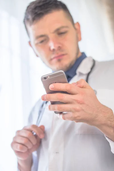 Young doctor with stethoscope on the neck using smartphone