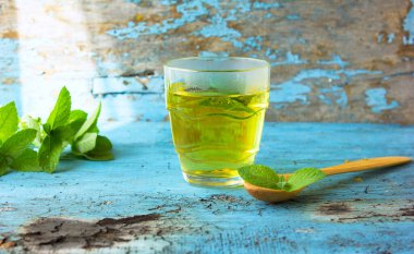 Ahşap bir masada bir bardak bitkisel Melissa naneli çayı. Melissa naneli çayı şeffaf bir fincanda, ahşap masada nane çiçekleri. Bebeğin midesi için bitki çayı, karın ağrısı. Sakinleştirici. Kopyalama alanı.