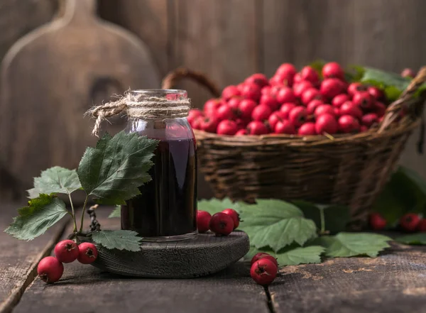 Hawthorn berries  tincture or infusion bottle and basket of thorn apples on wooden board. Herbal medicine.