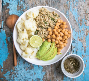 Bir kase sağlıklı vegan ve vejetaryen yemeği veya akşam yemeği. Kızarmış nohut salatası, kinoa, avokado, arka planda karnabahar.