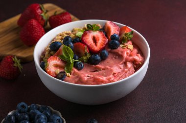 Fresh acai smoothie bowl topped with strawberries, blueberries, and crunchy granola, healthy vegan breakfast.