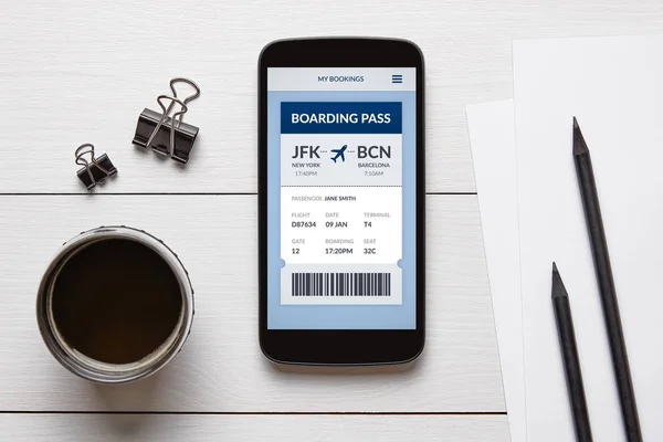 Boarding pass concept on smart phone screen with office objects on white wooden table. All screen content is designed by me. Flat lay