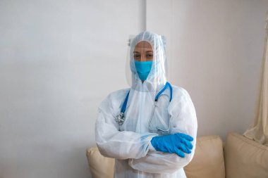 Koruyucu giysili, tıbbi maskeli, kollarını kavuşturmuş bir kadın. Sosyal izolasyon kavramı
