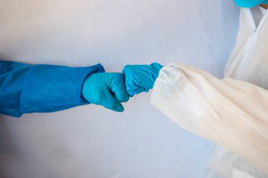 Tıbbi eldivenli eller beyaz arka planda yumruk tokuşturarak birbirini selamlıyor..