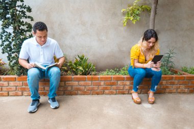 Parkta oturan maskeli iki Latin uzak duruyor ve kendilerini COVID-19 virüsünden koruyorlar. Sosyal uzaklık kavramı
