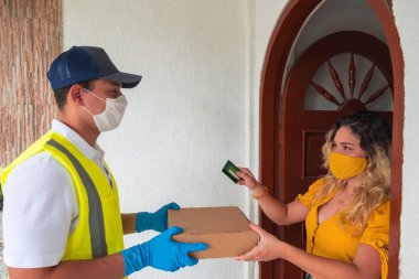 Maske takan Latin kurye bir karton teslim ediyor. Müşterinin evinde Coronavirus önleme.