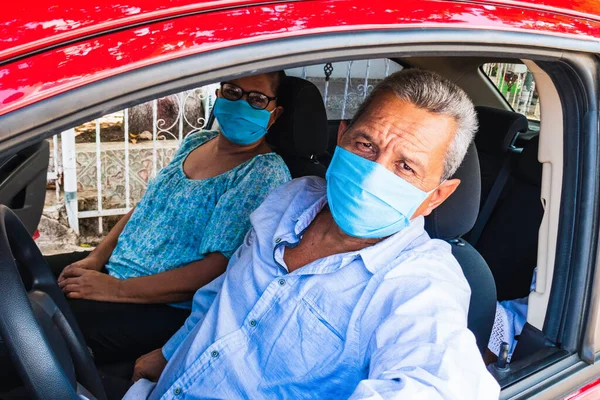 An elderly man in a medical face mask driving a car. Coronavirus pandemic concept. Road trip, travel and old people concept - happy senior couple driving in car