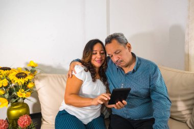 Yaşlı çift evdeki kanepede kitap okuyor.