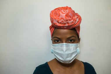 Evde başörtüsü ve tıbbi maske takan zarif giyimli bir Afrikalı kadın. Salgın konsepti