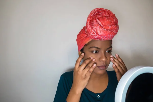 A beautiful young African-American woman applying body cream. Beauty and skin care routine.