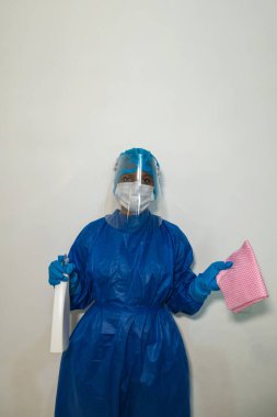 Mavi koruyucu takım elbiseli, orta boy maskeli, lastik eldivenli ve gözlüklü bir kadın. Ellerinde sıvı spreyi var. Dezenfeksiyon konsepti, COVID-19 virüsüyle mücadele.
