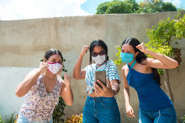 Tre Latinamerikanska Vänner Ansiktsmasker Ser Förvånad Och Upphetsad Mobiltelefon — Stockfoto