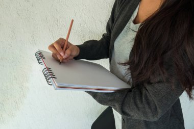 Kadın elinde defter tutuyor ve bir şeyler yazıyor.