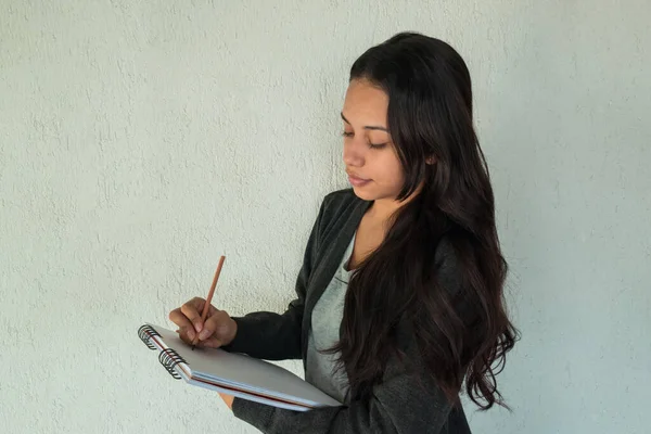 A charming young entrepreneur taking notes in a notebook smiling on a white background. Beautiful young student taking notes with a smile.
