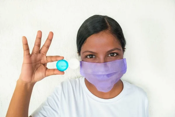 Maskeli genç bir kadın, görüş için konteynır ve lens tutuyor. Yüz maskesi takıyor.