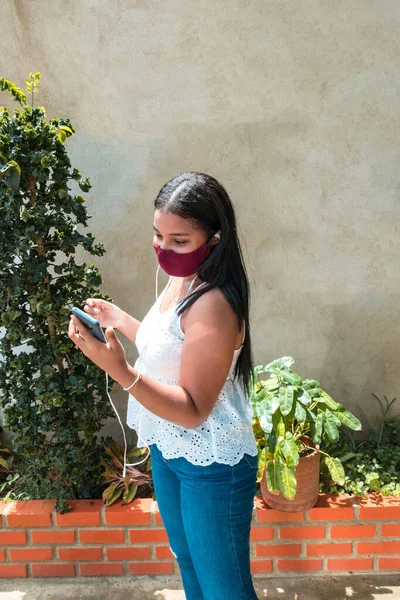 Woman with mask listening to music on her cell phone and dancing in her backyard