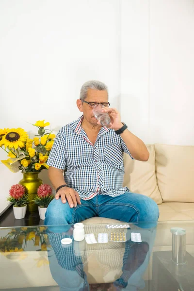 Older man taking medicine in the living room at home.