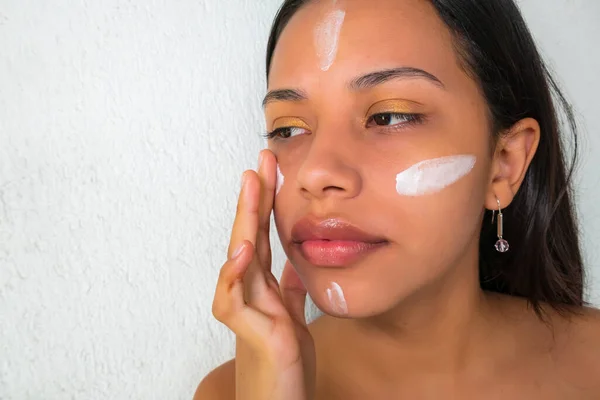 Çekici genç esmer, çıplak omuzlu, yüzüne krem sürüyor.