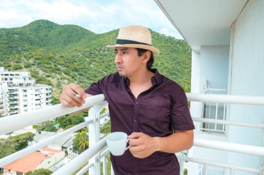 30 yaşında bir adam evinin balkonunda, rahat ve mutlu, bir fincan kahvenin ve sigara içmenin tadını çıkarıyor.