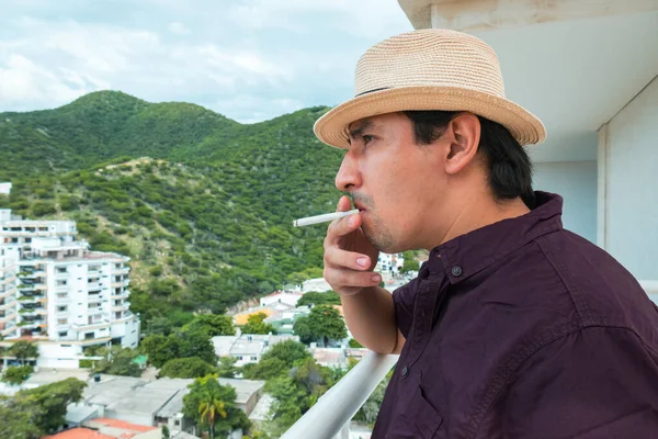 Genç adam balkonunda sigara içiyor.