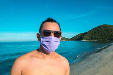 Sahildeki salgın için güneş gözlüklü ve maskeli adam.