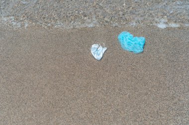 Virüs koruyucu maskeler ve kumlu deniz kıyısında tıbbi kapaklar, koronavirüs kirliliği hastalığı