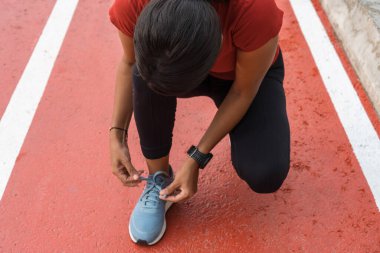 Koşucu, akıllı kalp atış hızı monitörünü kullanarak ayakkabı bağcıklarını yarış pistinde bağlıyor. Koşucular için koşu ayakkabıları ve spor saatleri