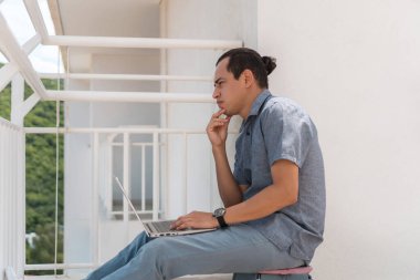 Düşünceli genç adam evinin balkonunda çalışırken gün batımını seyrediyor..