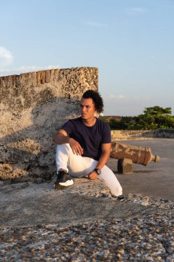 Genç adam eski bir taş kale duvarında oturuyor, günbatımının tadını çıkarıyor.