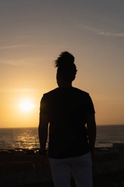 Huzurlu okyanusun üzerinde gün batımını seyreden kişi siluetli duruyor.