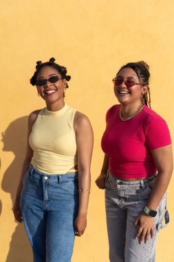 Sarı bir duvarın karşısında gülen ve eğlenen iki genç arkadaş.