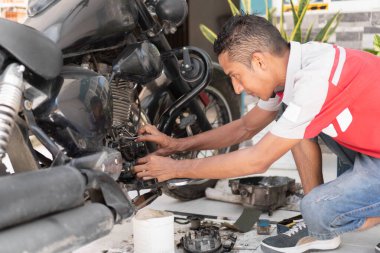 Motosiklet tamirine odaklanan bir adam garajda mekanik bakım yapıyor.