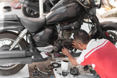 Tamirci garajda yerde motor tamir ediyor.